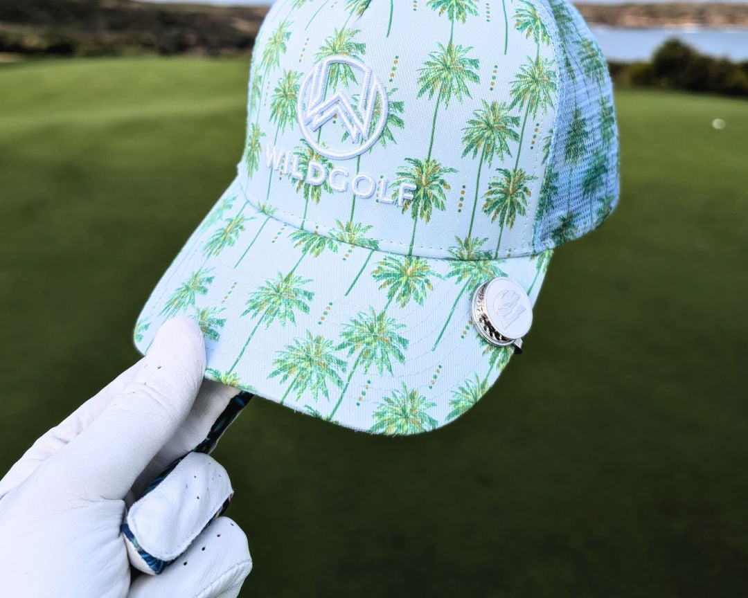 Golf cap with palm tree design held by a gloved hand on a golf course